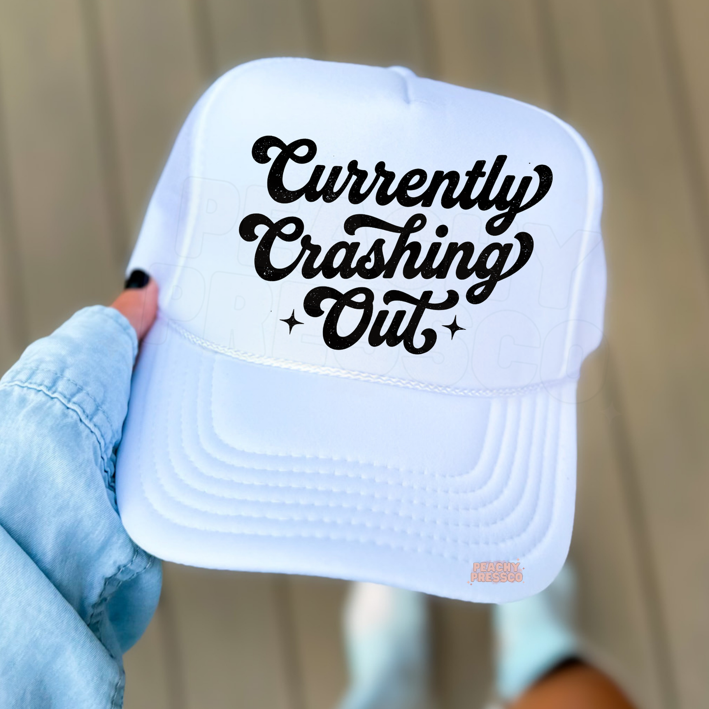 White trucker hat featuring “Currently Crashing Out” script text.
