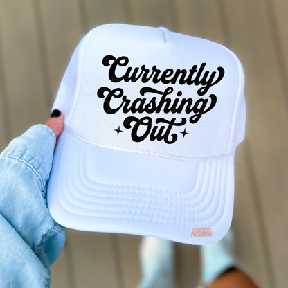 White trucker hat featuring “Currently Crashing Out” script text.
