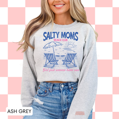 Woman wearing an ash grey sweatshirt with blue and pink beach club graphic and “Girls just wanna have sun” quote.