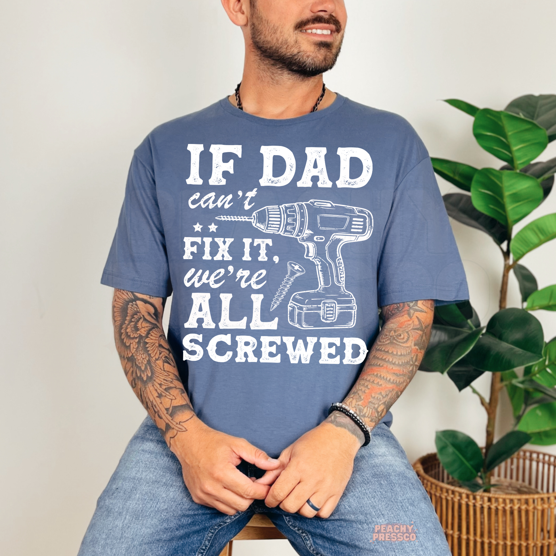 Smiling man wearing blue t-shirt with “If Dad Can’t Fix It, We’re All Screwed” handyman-themed graphic print.