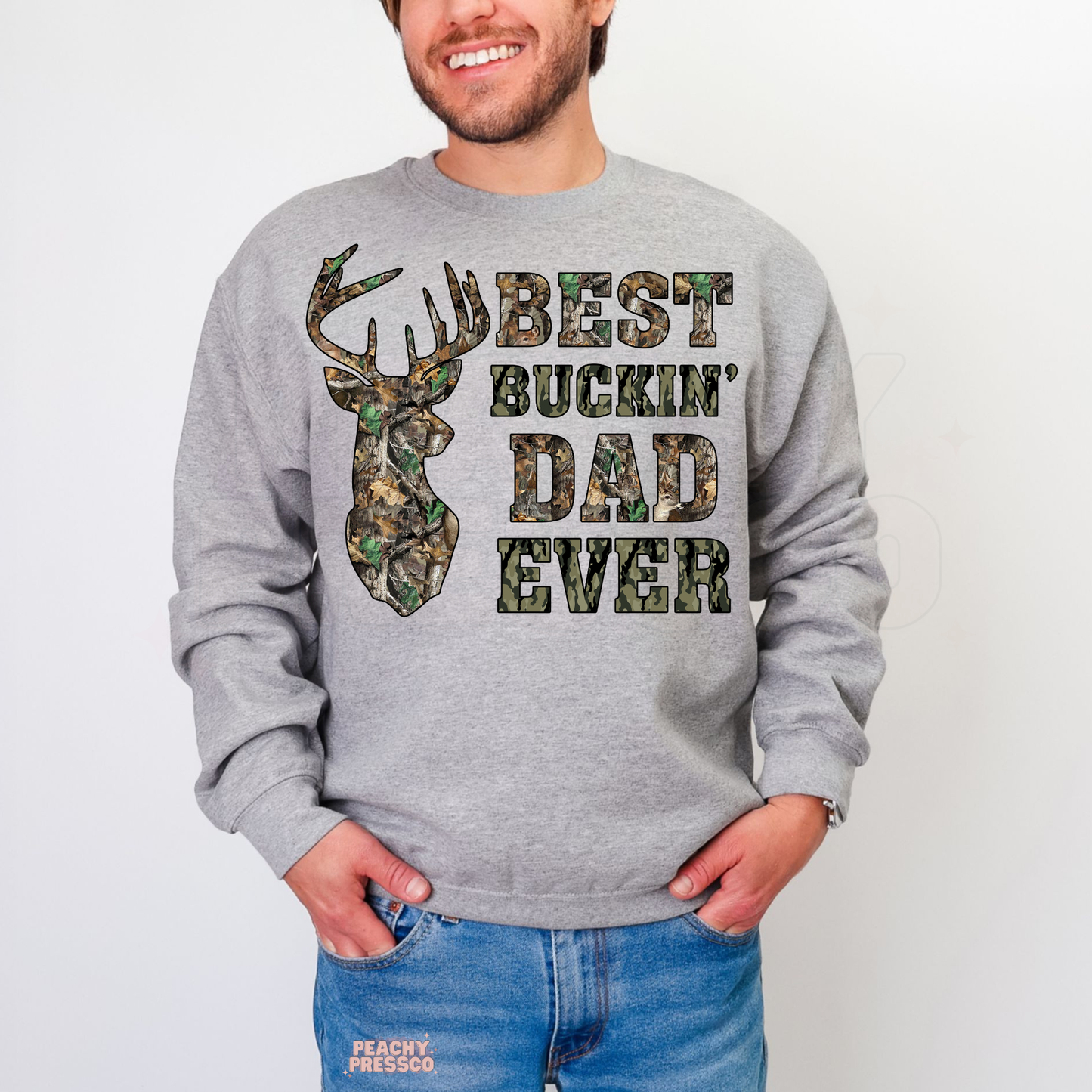 Man wearing grey crewneck sweatshirt with camouflage deer head graphic and “Best Buckin’ Dad Ever” text design.