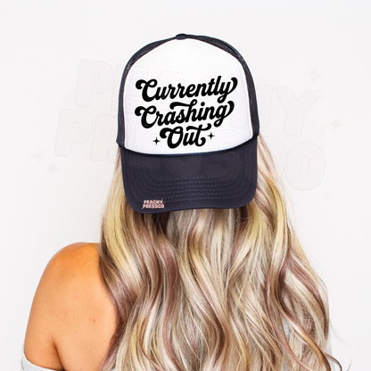 Navy and white trucker hat featuring “Currently Crashing Out” script text.
