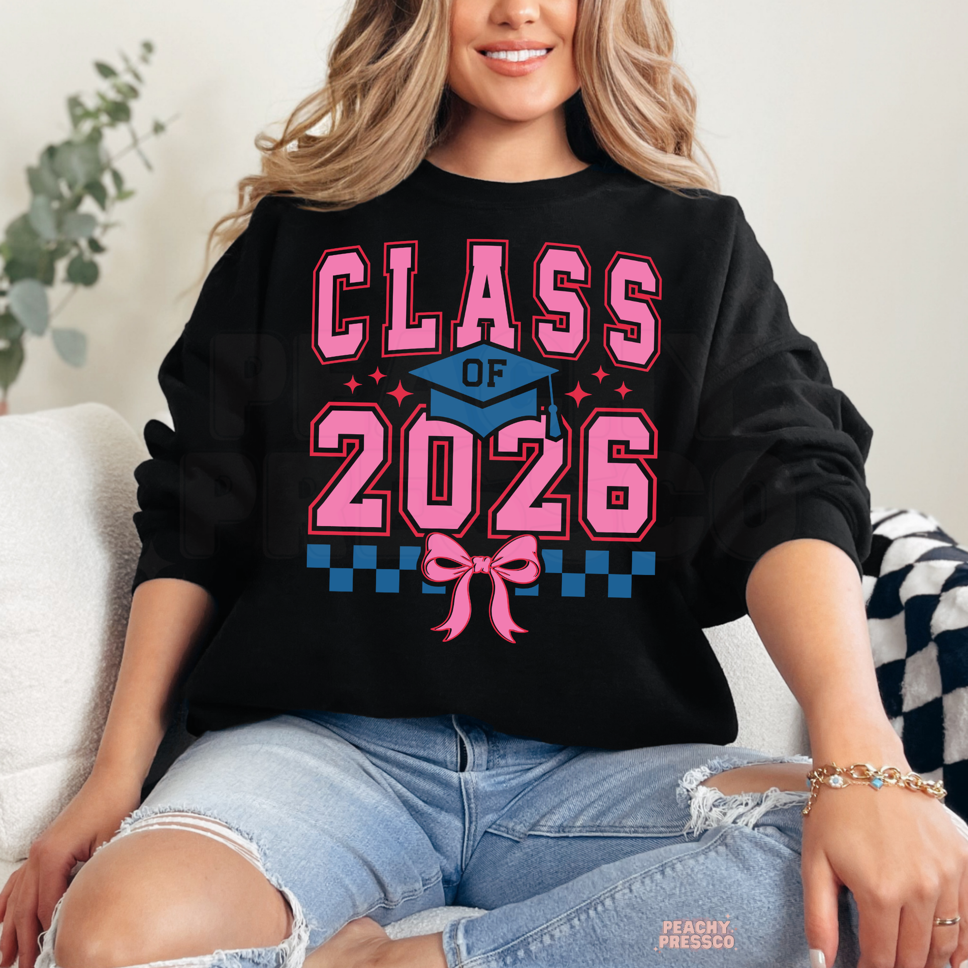 Class of 2026 coquette graduation crewneck featuring pink varsity text, graduation cap, bow detail, and grad year apparel.