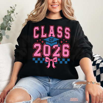 Class of 2026 coquette graduation crewneck featuring pink varsity text, graduation cap, bow detail, and grad year apparel.