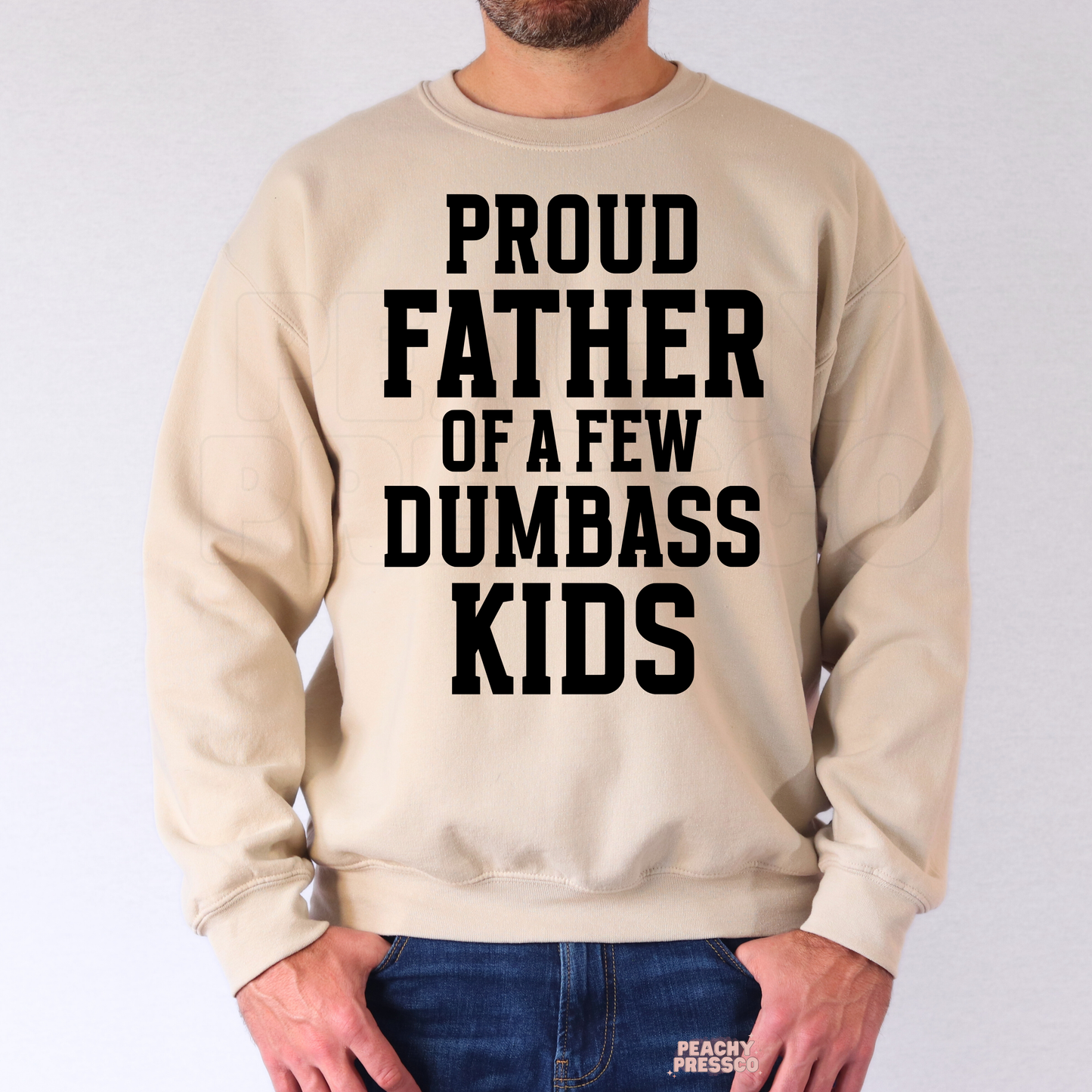 Man wearing beige crewneck sweatshirt with bold black “Proud Father of a Few Dumbass Kids” graphic design.