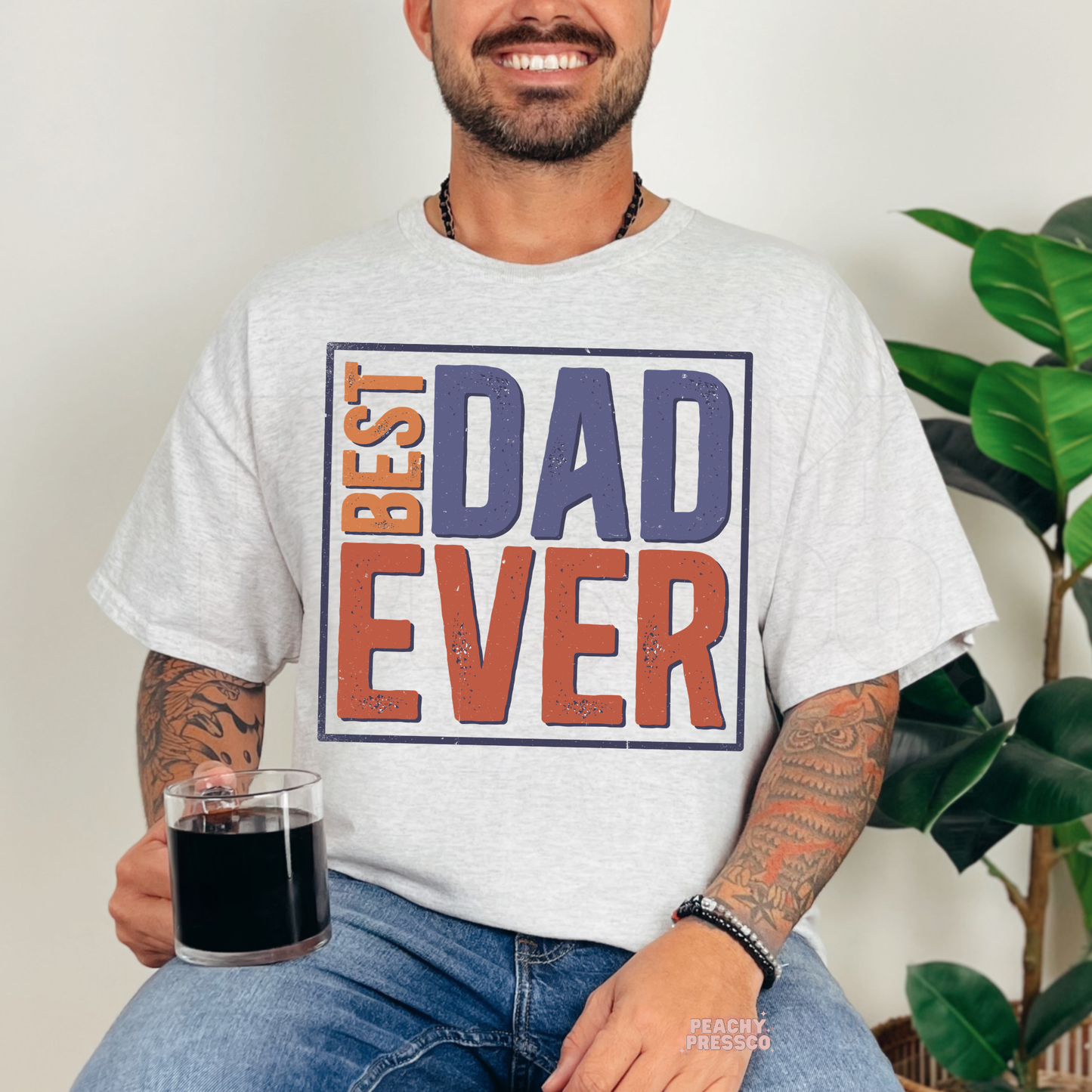 Man sitting indoors wearing ash grey t-shirt featuring retro “Best Dad Ever” Father’s Day graphic design.