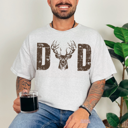 Smiling man modeling ash grey t-shirt featuring deer head antler “DAD” graphic in vintage distressed style.