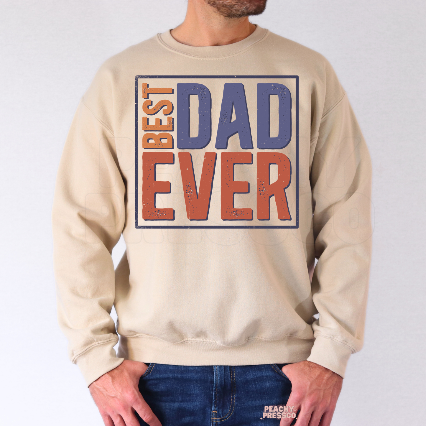 Man wearing beige sweatshirt with distressed retro “Best Dad Ever” text graphic in muted blue and orange colors.