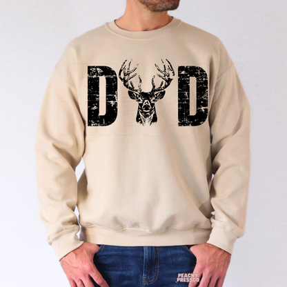 Man wearing beige crewneck sweatshirt with rustic deer antler dad graphic and distressed black lettering.
