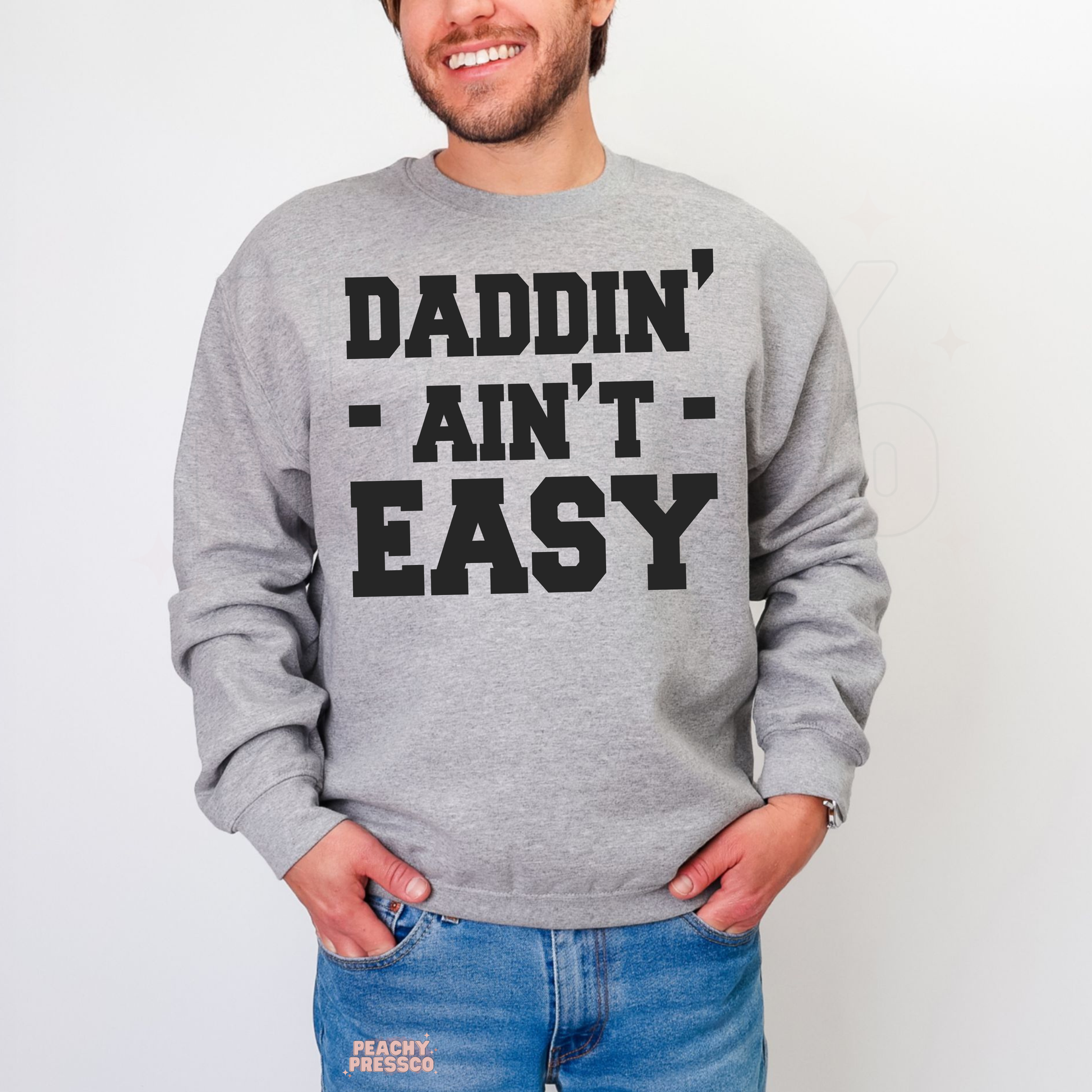 Man modeling grey sweatshirt with bold western-style “Daddin’ Ain’t Easy” typography design.