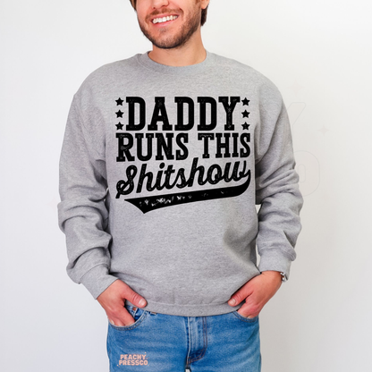 Man modeling grey crewneck sweatshirt with funny dad quote “Daddy Runs This Shitshow” in bold black lettering.