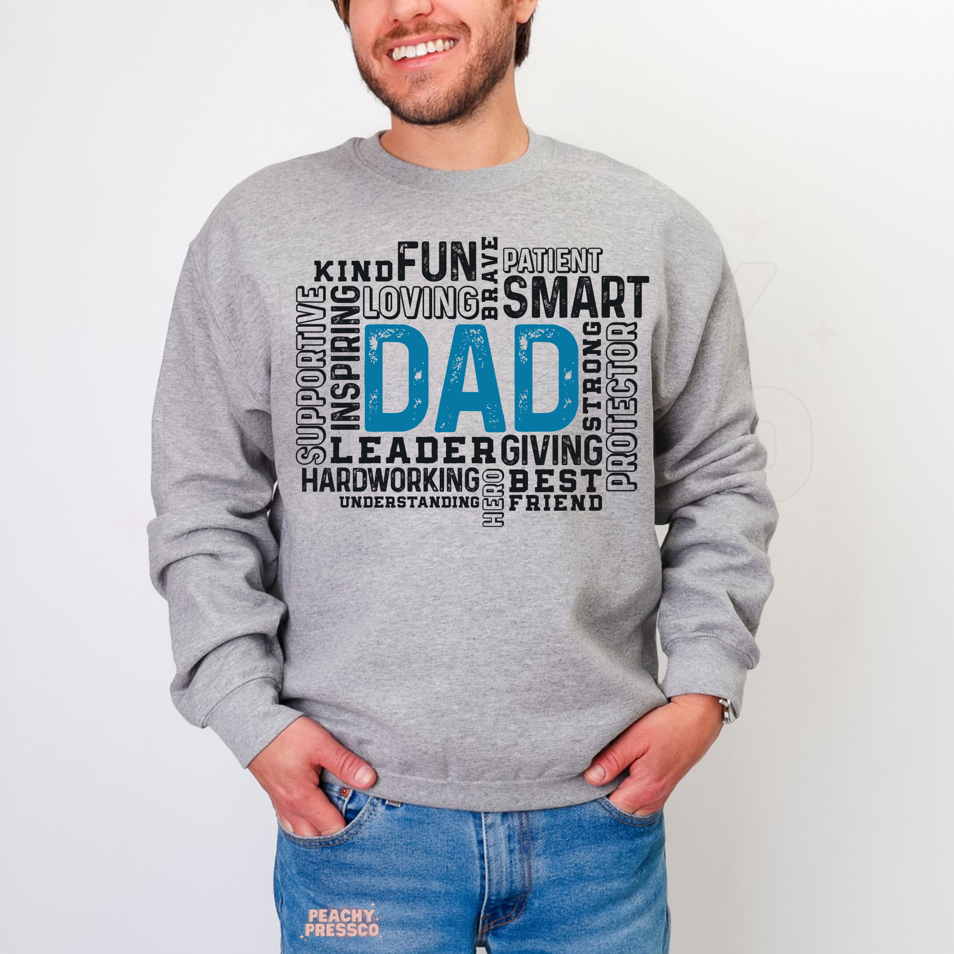 Man modeling light grey crewneck sweatshirt with inspirational “Dad” word collage graphic including words like strong, smart, loving, and protector.