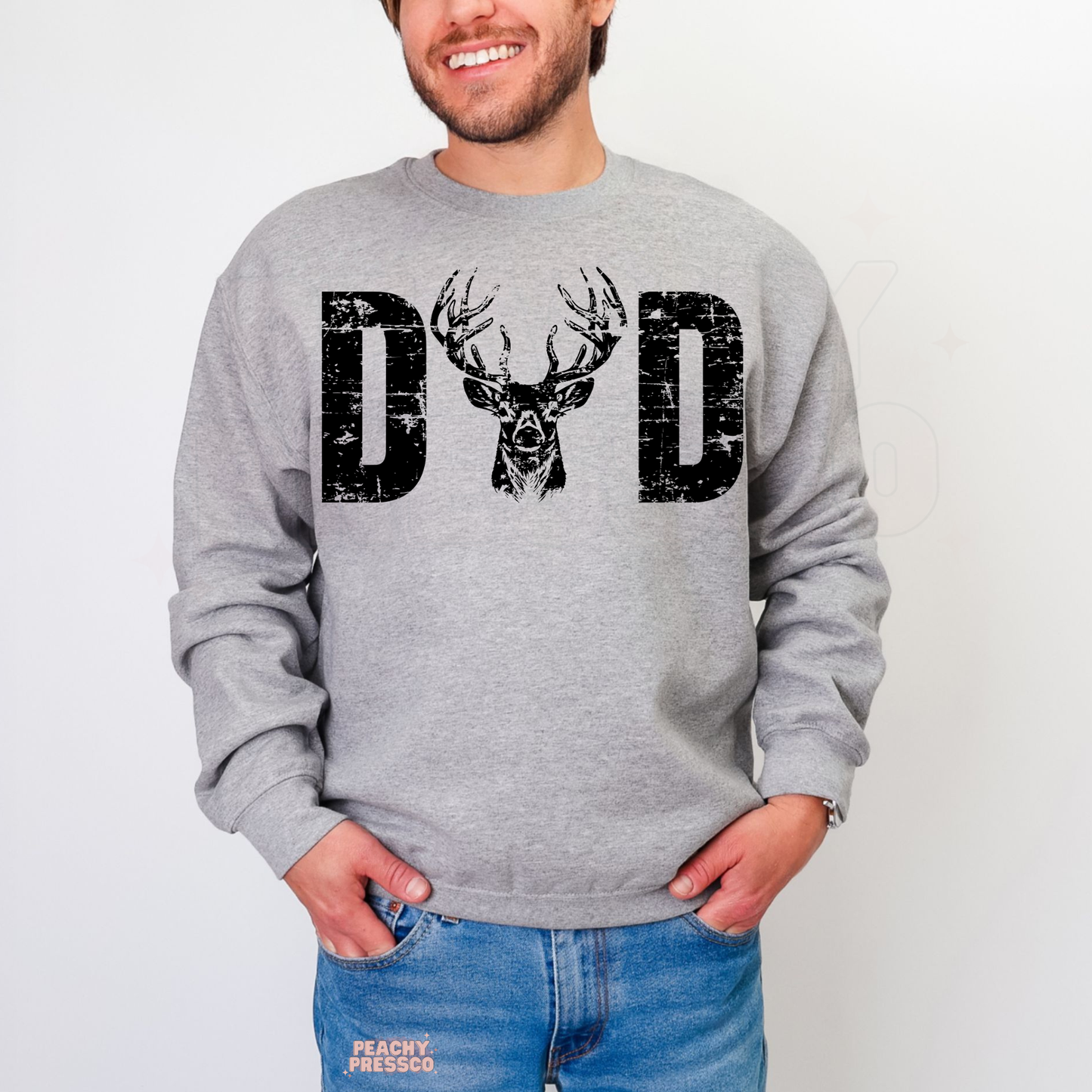 Man modeling grey crewneck sweatshirt with bold distressed “DAD” hunting graphic featuring buck deer illustration.