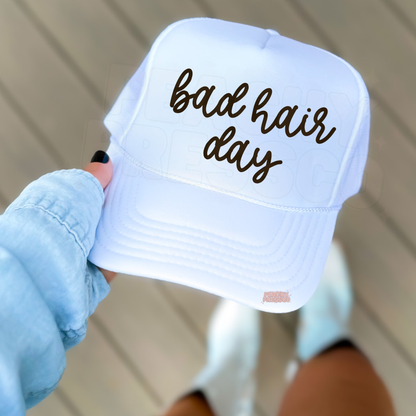 White trucker hat featuring handwritten “Bad Hair Day” graphic.