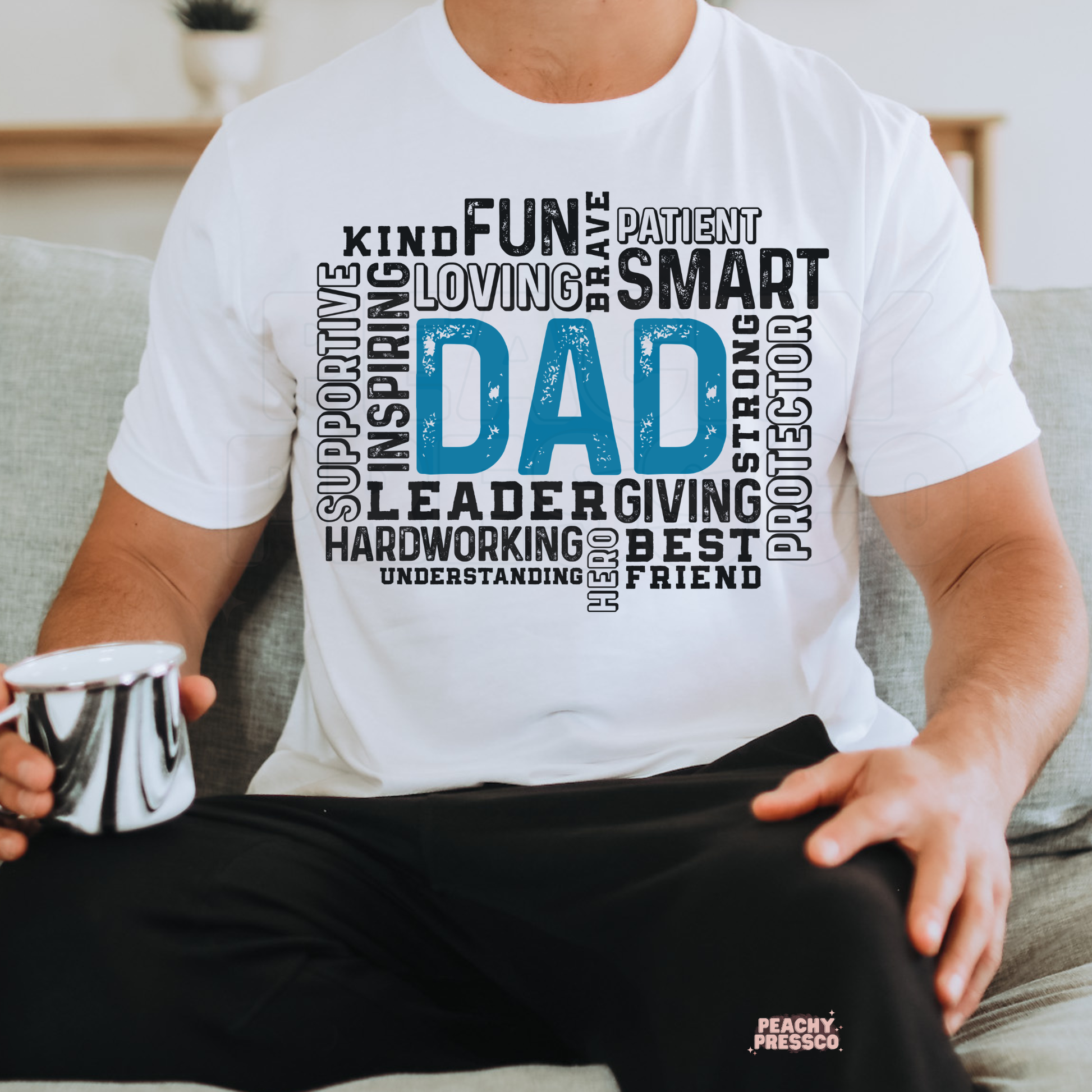 Man sitting on couch wearing white t-shirt with blue “Dad” word art and positive descriptive words.

