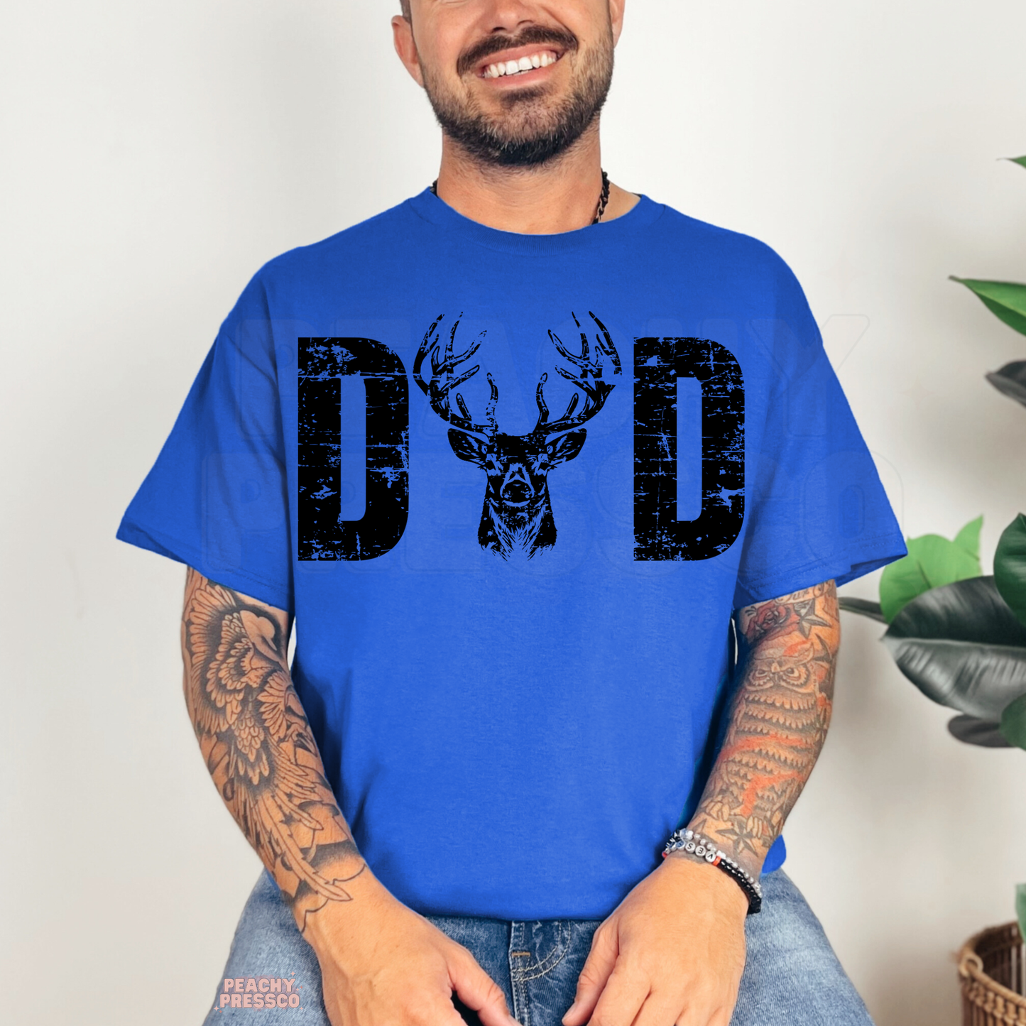 Smiling man wearing royal blue t-shirt with black distressed deer antler dad graphic design.