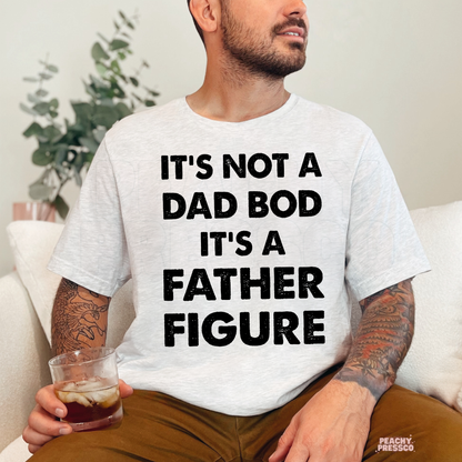 Man sitting indoors wearing ash grey t-shirt featuring humorous “Father Figure” dad quote graphic.