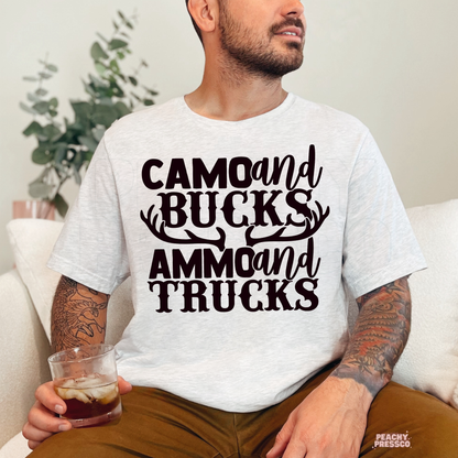 Man sitting indoors wearing ash grey t-shirt with deer antler “Camo and Bucks Ammo and Trucks” graphic design.