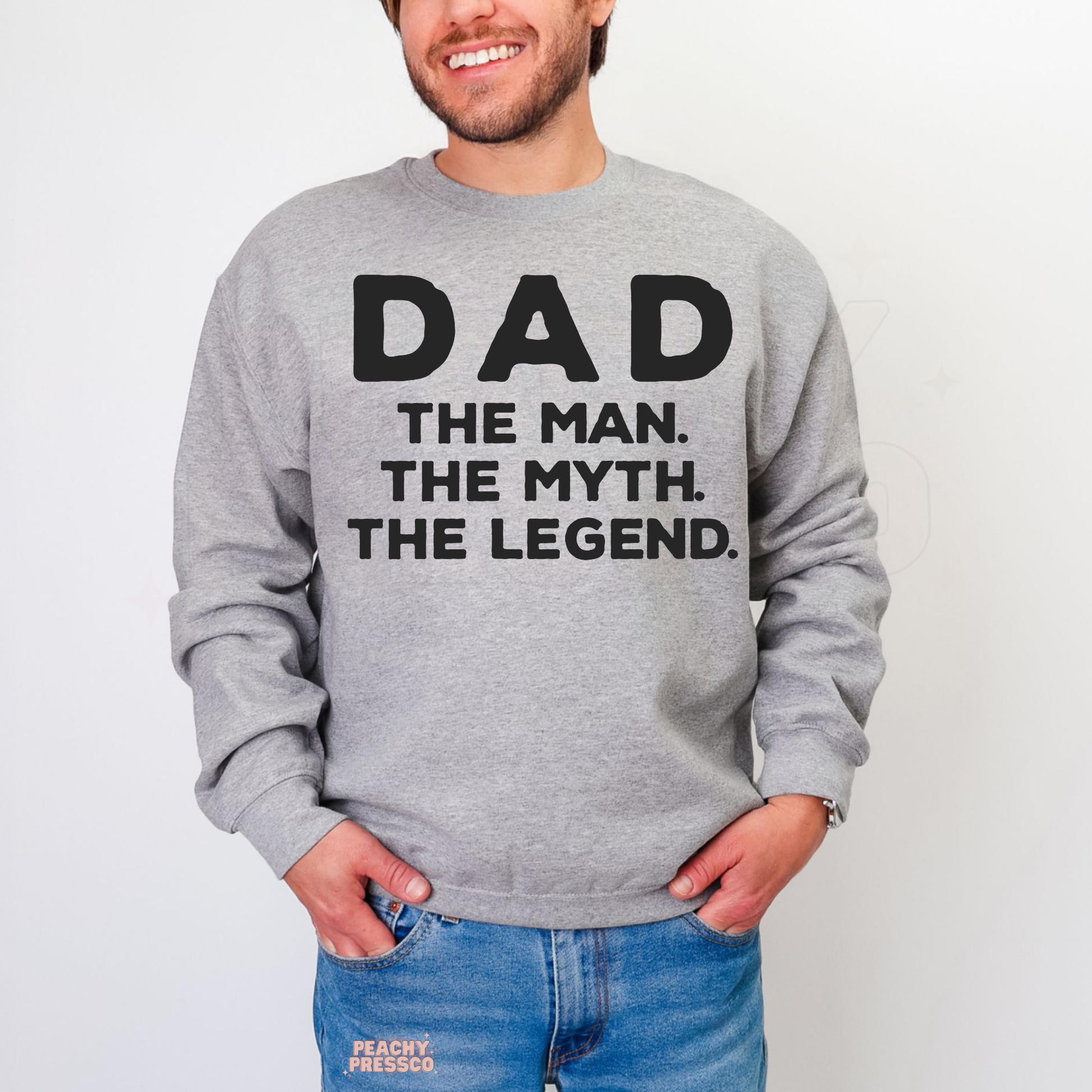 Man modeling grey crewneck sweatshirt featuring black “Dad The Man. The Myth. The Legend.” slogan design.