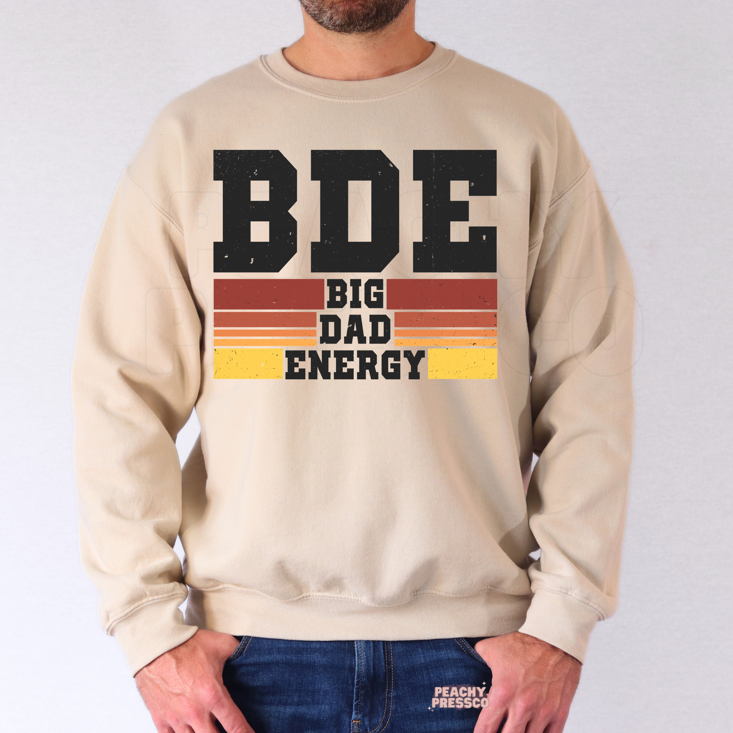 Man modeling beige crewneck sweatshirt with vintage “Big Dad Energy” graphic and sunset stripe details.