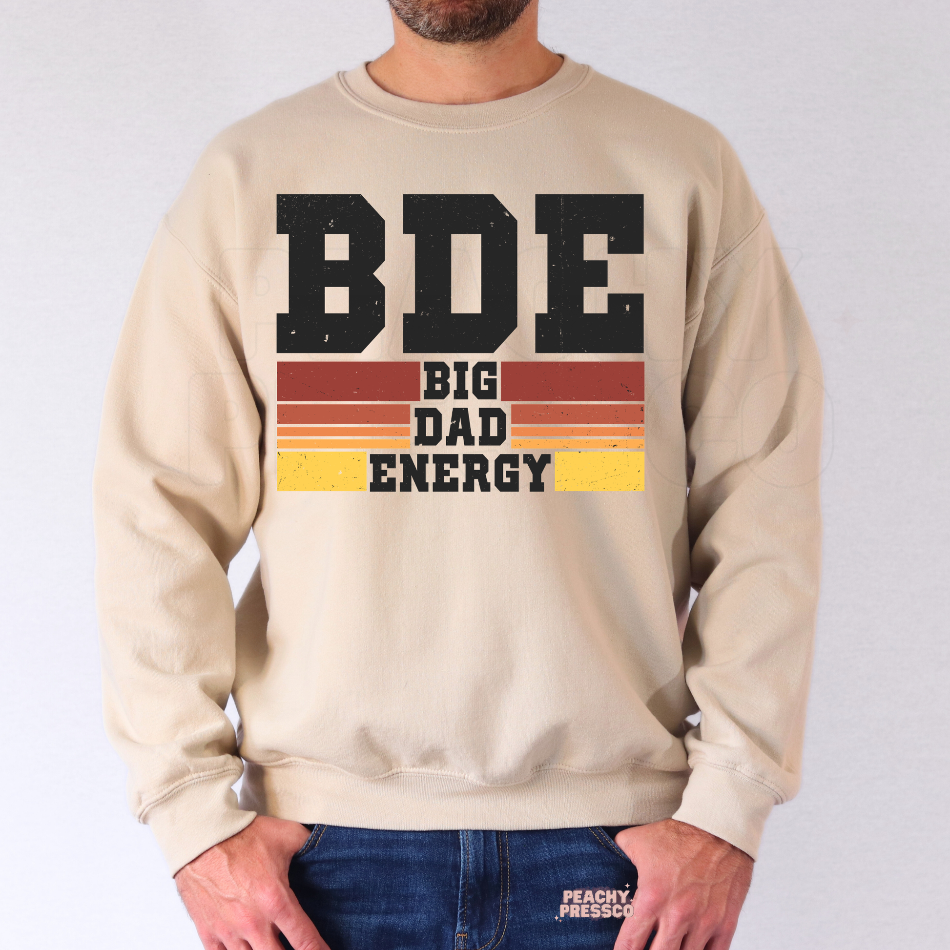Man modeling beige crewneck sweatshirt with vintage “Big Dad Energy” graphic and sunset stripe details.