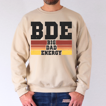Man modeling beige crewneck sweatshirt with vintage “Big Dad Energy” graphic and sunset stripe details.