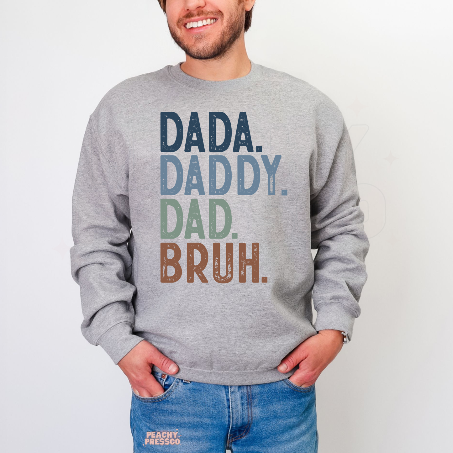 Man wearing grey crewneck sweatshirt with retro-style “Dada Daddy Dad Bruh” dad life graphic print.