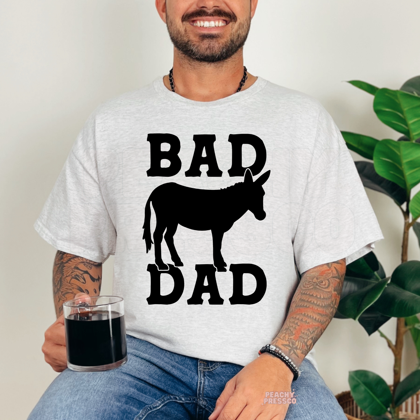 Man wearing ash grey t-shirt featuring black “Bad Dad” typography and donkey silhouette graphic design.