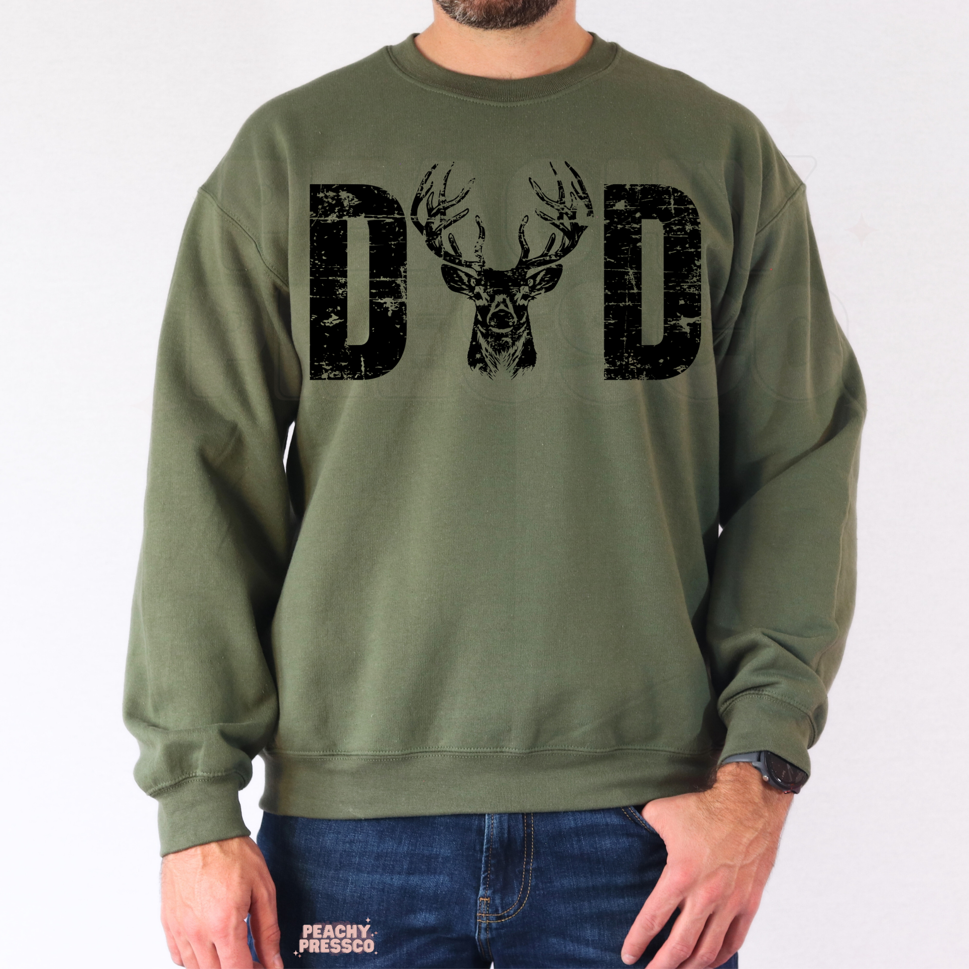 Man wearing military green crewneck sweatshirt with rustic “DAD” deer hunting graphic and distressed print style.