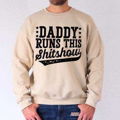 Man modeling beige crewneck sweatshirt with bold “Daddy Runs This Shitshow” dad-themed graphic design.