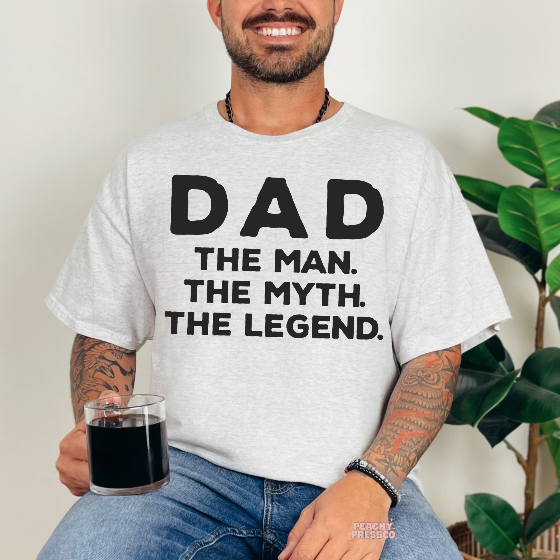 Smiling man wearing ash grey t-shirt with oversized “Dad The Man. The Myth. The Legend.” Father’s Day graphic.