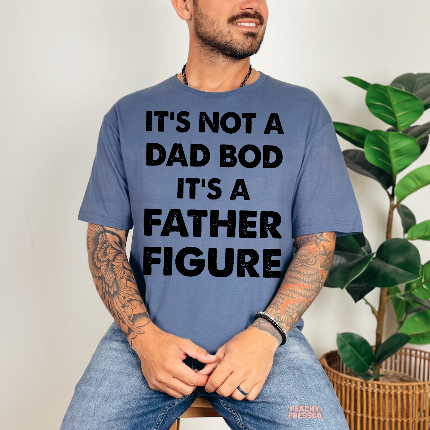 Man wearing blue t-shirt with funny dad saying “It’s Not a Dad Bod It’s a Father Figure” in distressed black text.