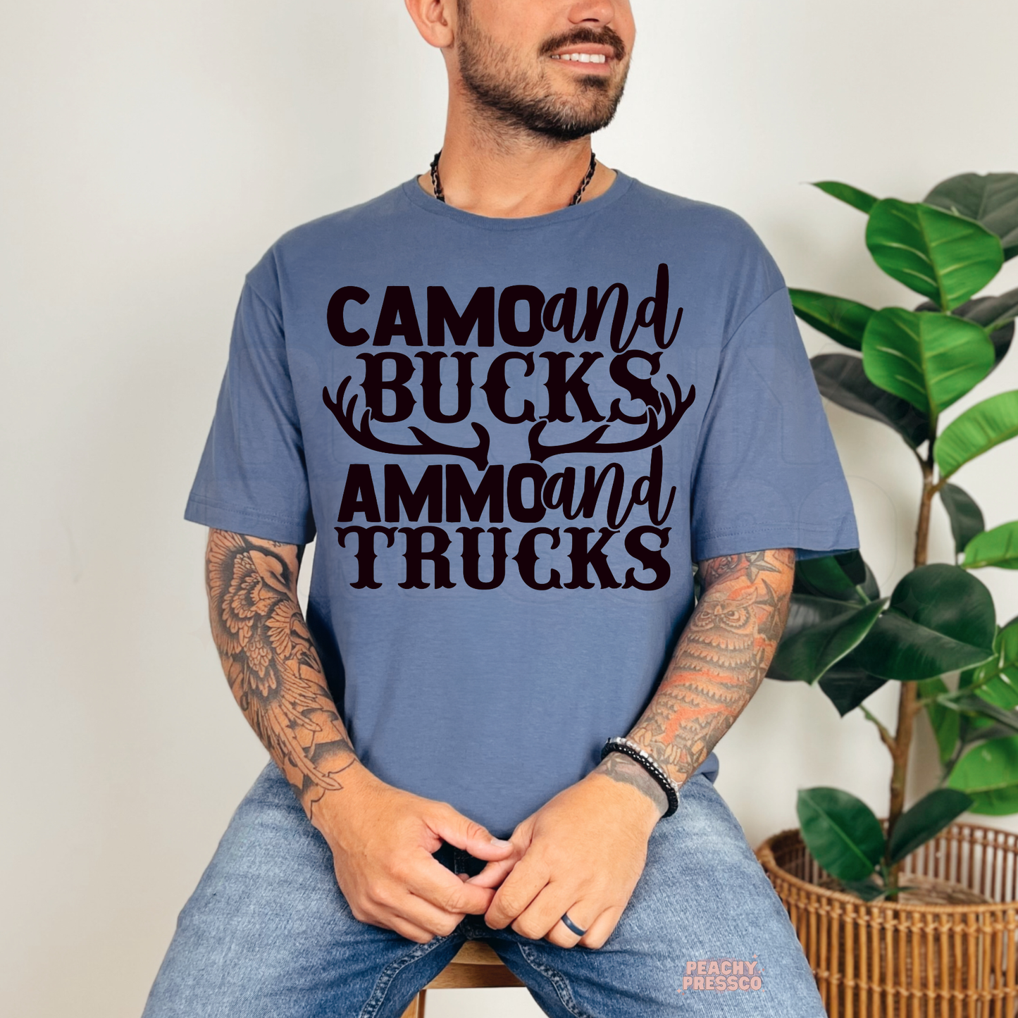 Man wearing blue t-shirt featuring rustic deer antler “Camo and Bucks Ammo and Trucks” graphic print.