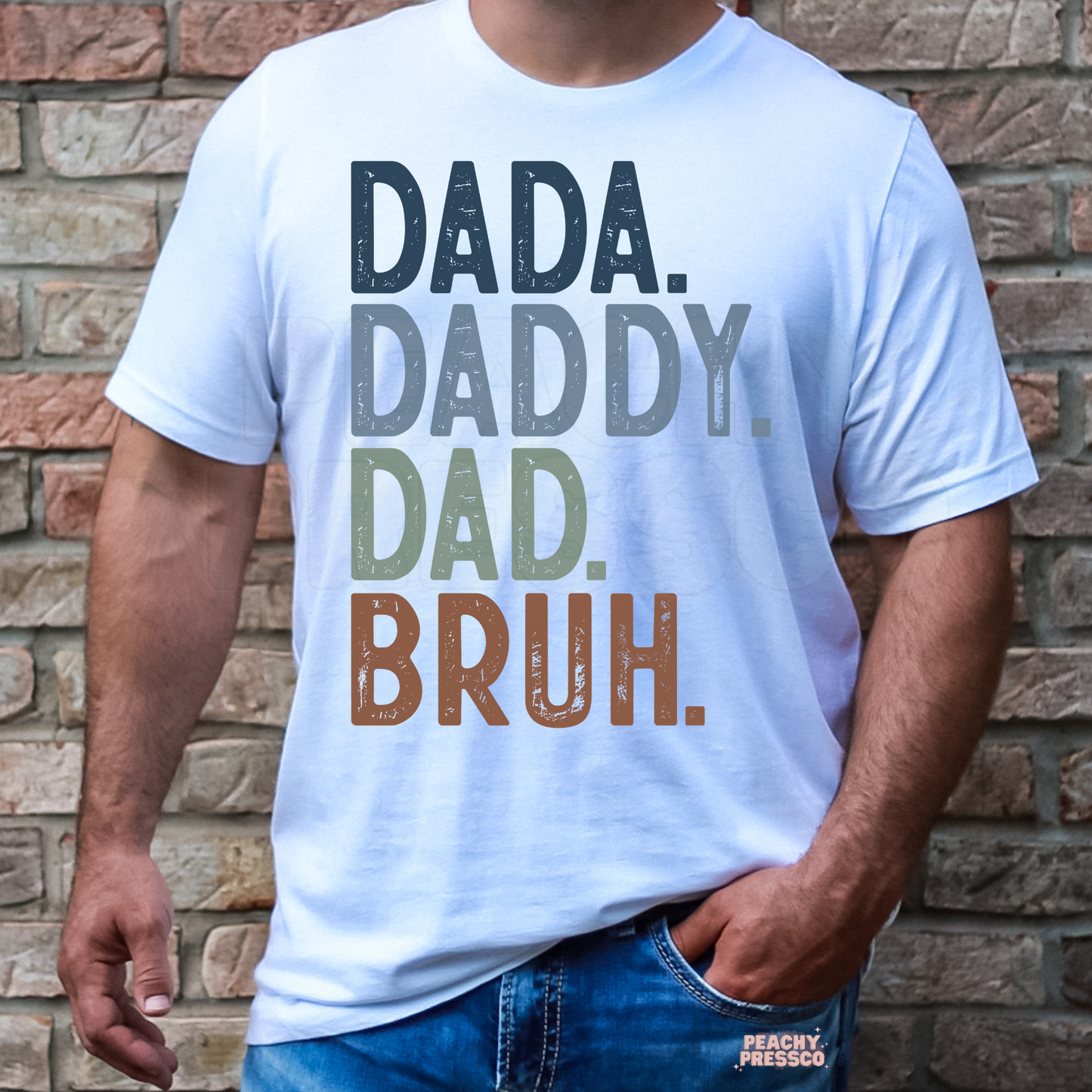 Man wearing white t-shirt with stacked “Dada Daddy Dad Bruh” typography graphic in muted colors.
