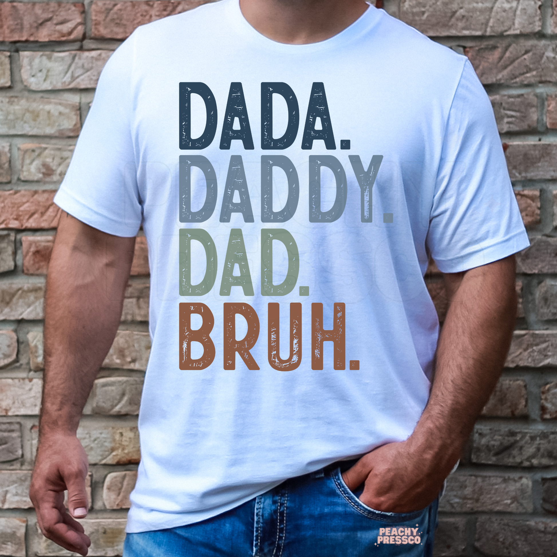 Man wearing white t-shirt with stacked “Dada Daddy Dad Bruh” typography graphic in muted colors.
