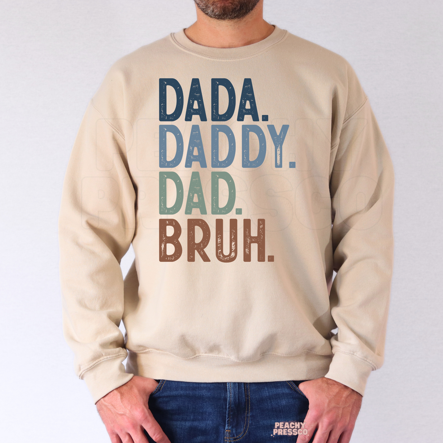 Man wearing beige crewneck sweatshirt featuring colorful “Dada Daddy Dad Bruh” funny Father’s Day design.