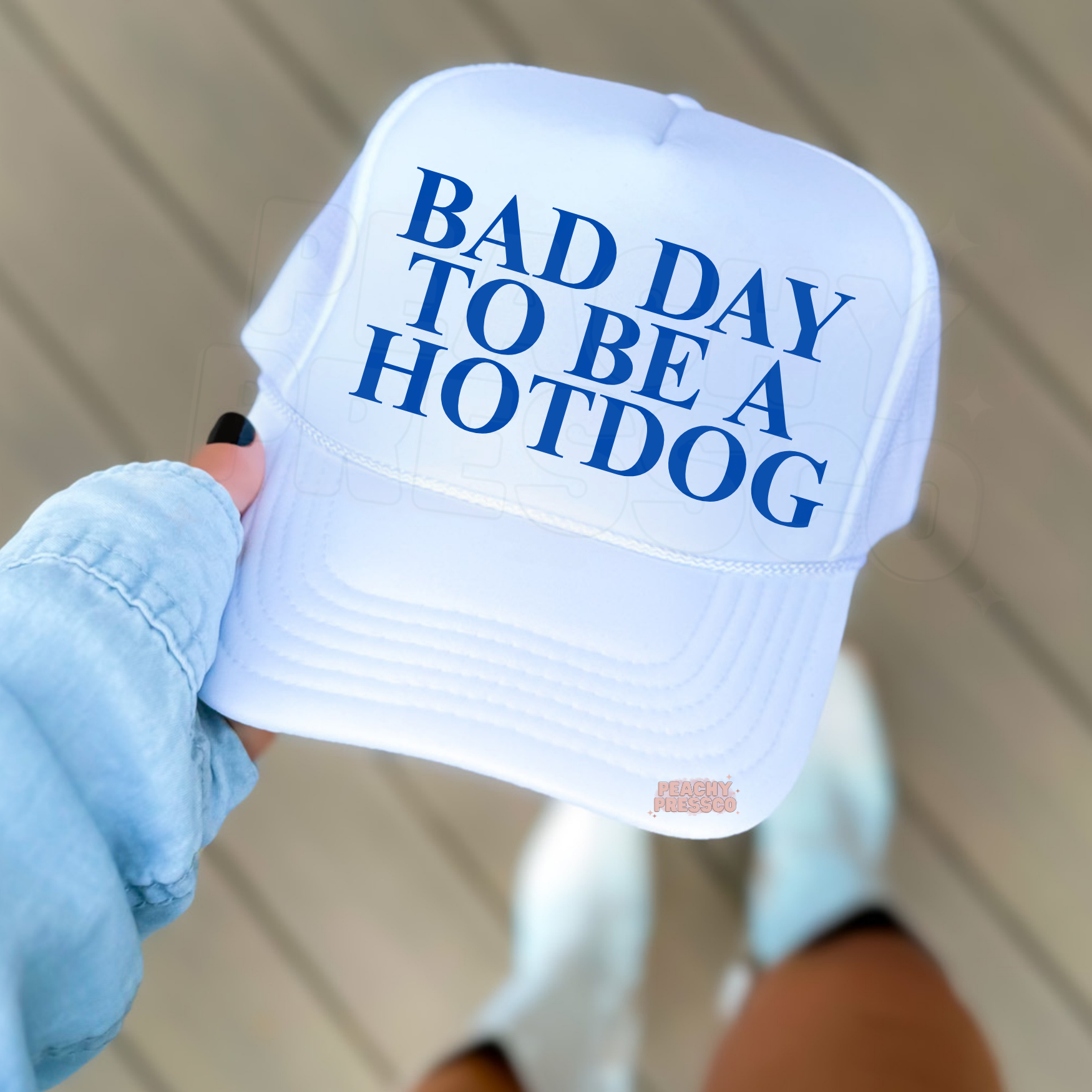 White foam trucker hatfeaturing bold royal blue text “BAD DAY TO BE A HOTDOG”. Casual summer lifestyle 