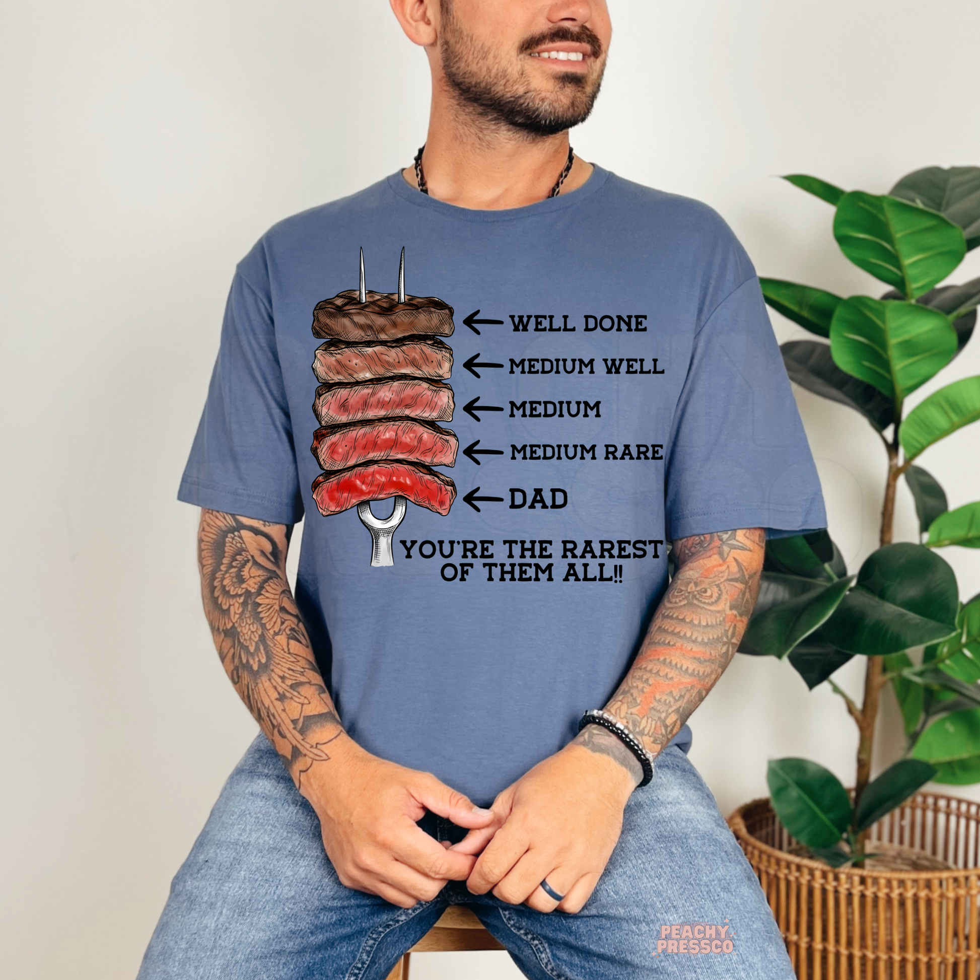 Smiling man in blue t-shirt featuring steak doneness illustration and humorous “Dad You’re the Rarest of Them All” graphic print.