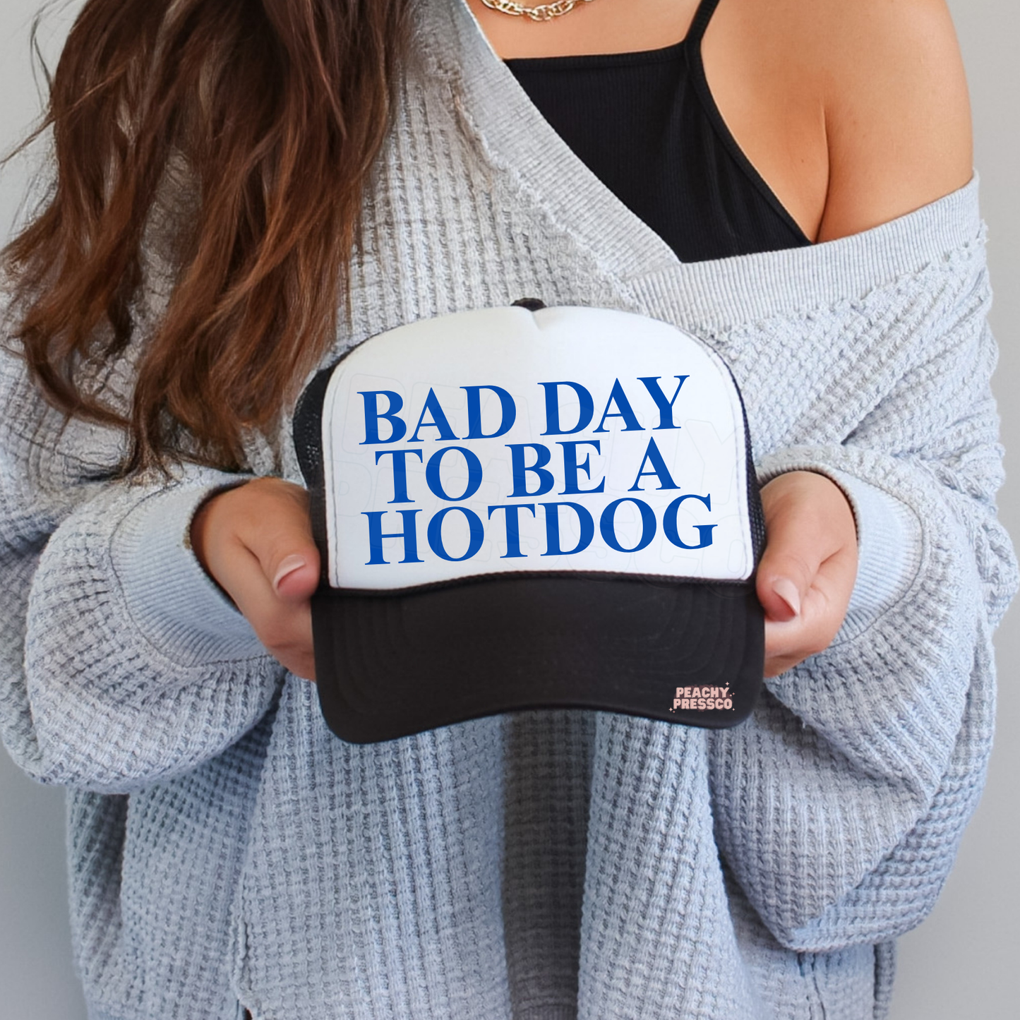 Black and white trucker hat featuring bold blue “BAD DAY TO BE A HOTDOG” typography. Trendy funny graphic trucker hat.