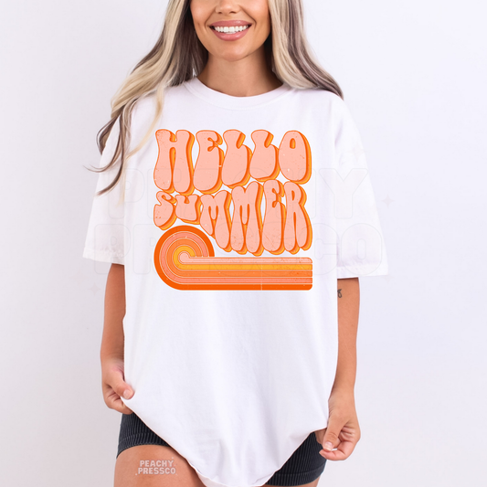 Woman wearing an oversized white graphic t-shirt featuring a retro “Hello Summer” design with peach bubble text and orange rainbow accents.