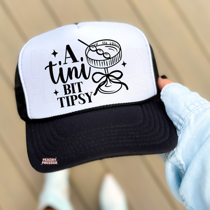 Woman wearing black and white trucker hat featuring “A Tiny Bit Tipsy” martini design, cute funny women’s summer accessory for vacations and girls weekends.