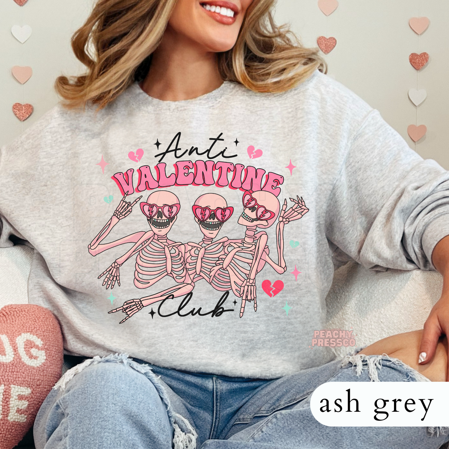Ash grey crewneck sweatshirt featuring the Anti Valentine Club skeleton trio wearing heart sunglasses with pink and mint Valentine's graphics for a cute spooky style.