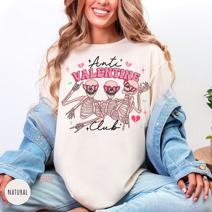Natural shirt featuring the "Anti Valentine Club" graphic with three pink skeletons wearing heart sunglasses, surrounded by broken hearts and sparkles.