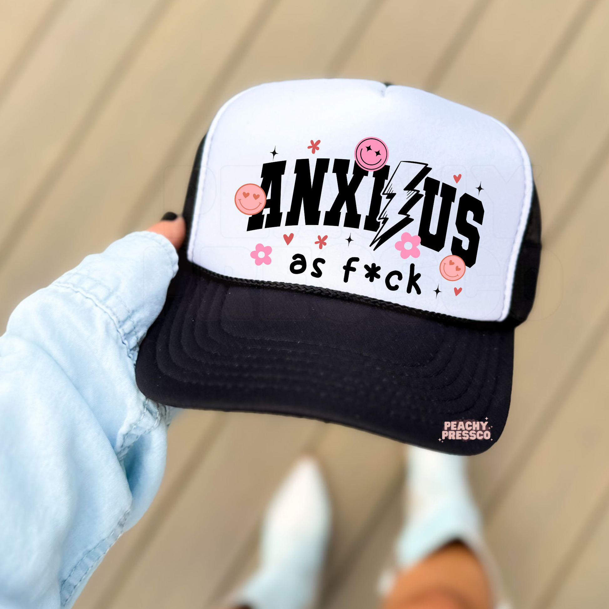White and black foam trucker hat featuring the phrase "Anxious as Fck" in bold black varsity lettering with a lightning bolt, pink smiley faces, flowers, hearts, and sparkles. Trendy funny anxiety trucker hat for everyday wear.*