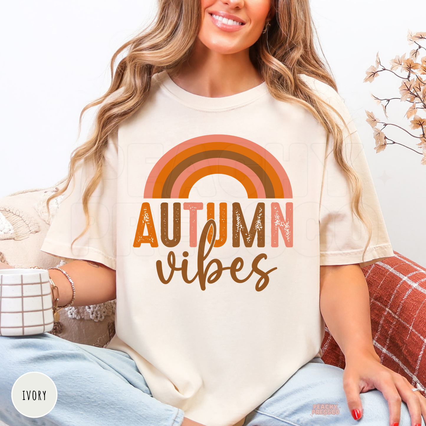 Woman wearing an ivory Comfort Colors t-shirt featuring a retro rainbow Autumn Vibes design in vintage orange, blush pink, and brown tones.