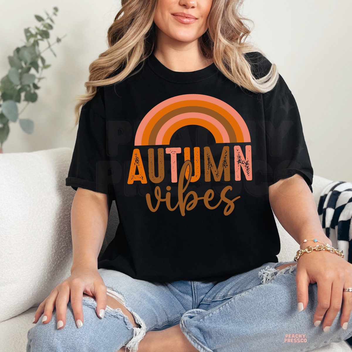 Woman wearing a black t-shirt featuring a retro rainbow "Autumn Vibes" graphic in warm orange and brown fall colors.