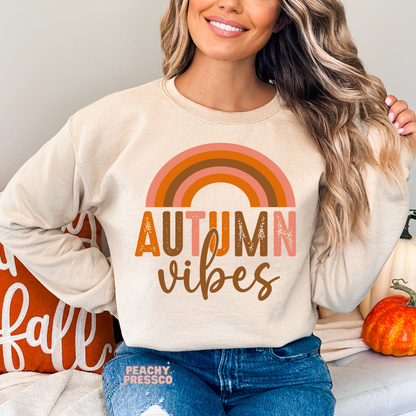 Woman wearing a sand crewneck sweatshirt with a retro autumn rainbow and Autumn Vibes graphic, perfect for pumpkin patch season and cozy fall outfits.