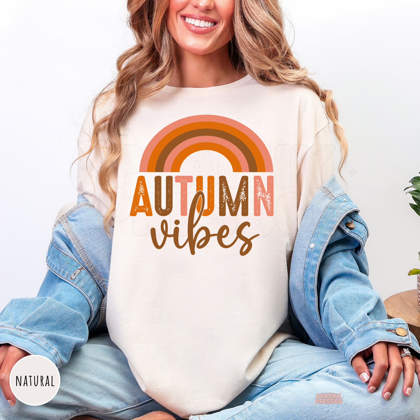 Woman wearing a natural shirt featuring a retro rainbow Autumn Vibes graphic in vintage-inspired autumn colors.