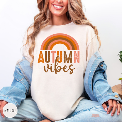 Woman wearing a natural shirt featuring a retro rainbow Autumn Vibes graphic in vintage-inspired autumn colors.