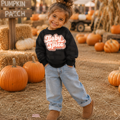 Cute toddler girl wearing a black "Baby Spice" sweatshirt with a retro leopard print graphic while posing at a pumpkin patch in autumn.